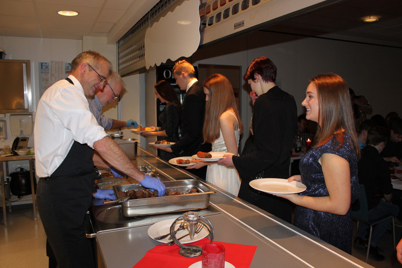 To tilsette serverer julemiddag til festkledde elevar. Foto: Stryn vgs