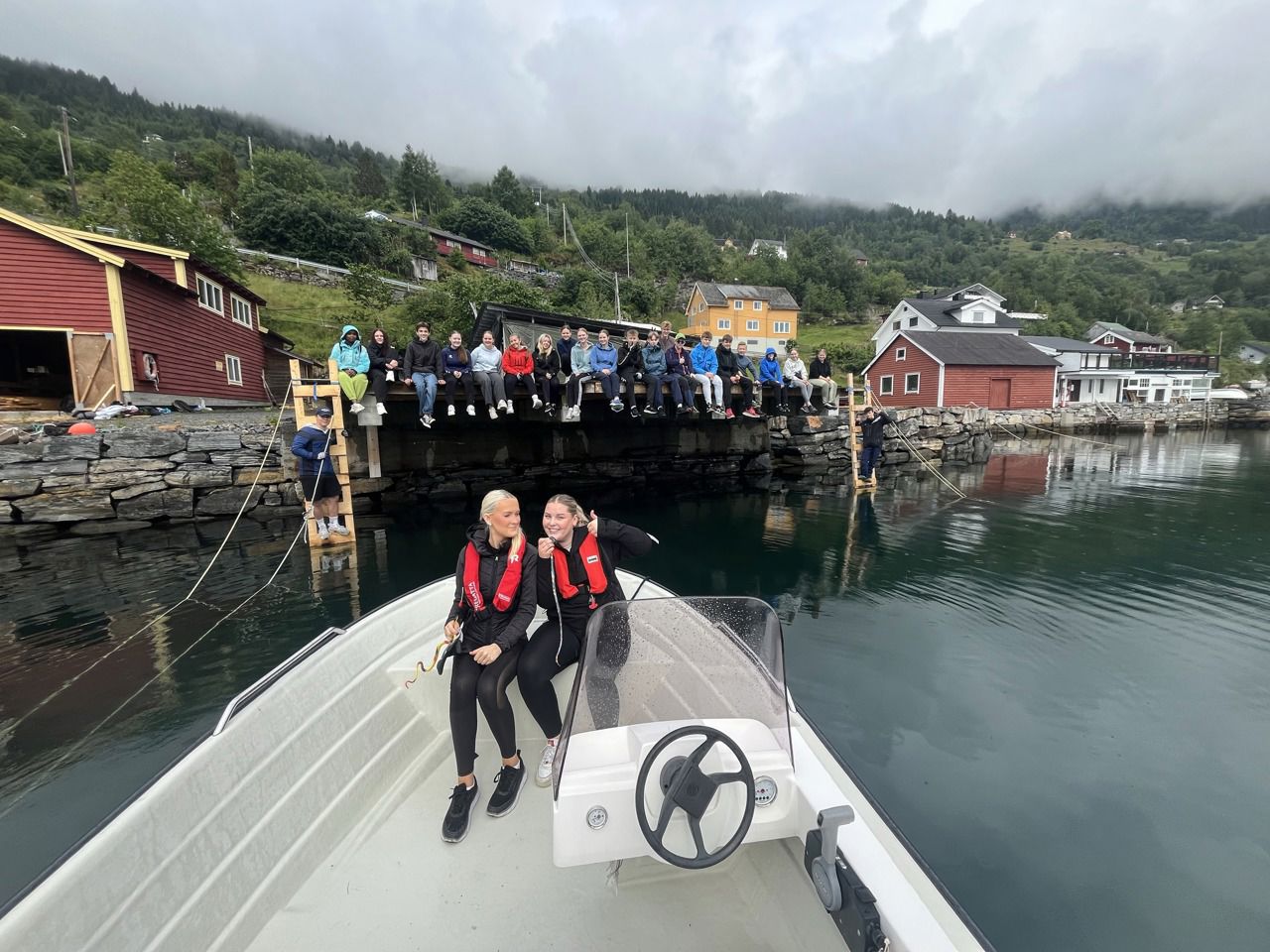 To personar i båt framfor mange personar på kaikanten. Foto: Stryn vgs