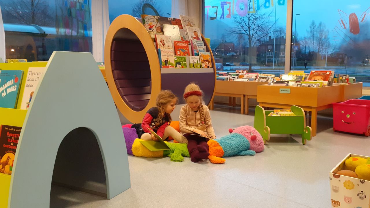 Bilde av to born som les på biblioteket